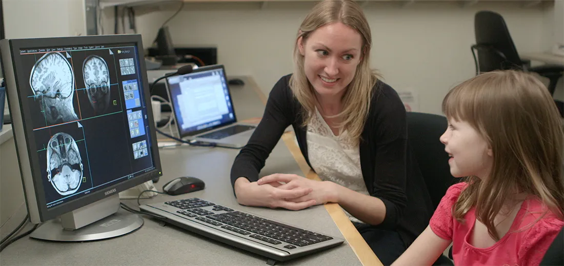 This image shows Dr. Richardson & a child viewing an image of the child's brain, together. After participating in an MRI study, children get to take home a picture of their brain.
