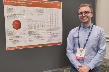 James Porter, a white male wearing a blue shirt, jeans and glasses, standing next to his poster presentation